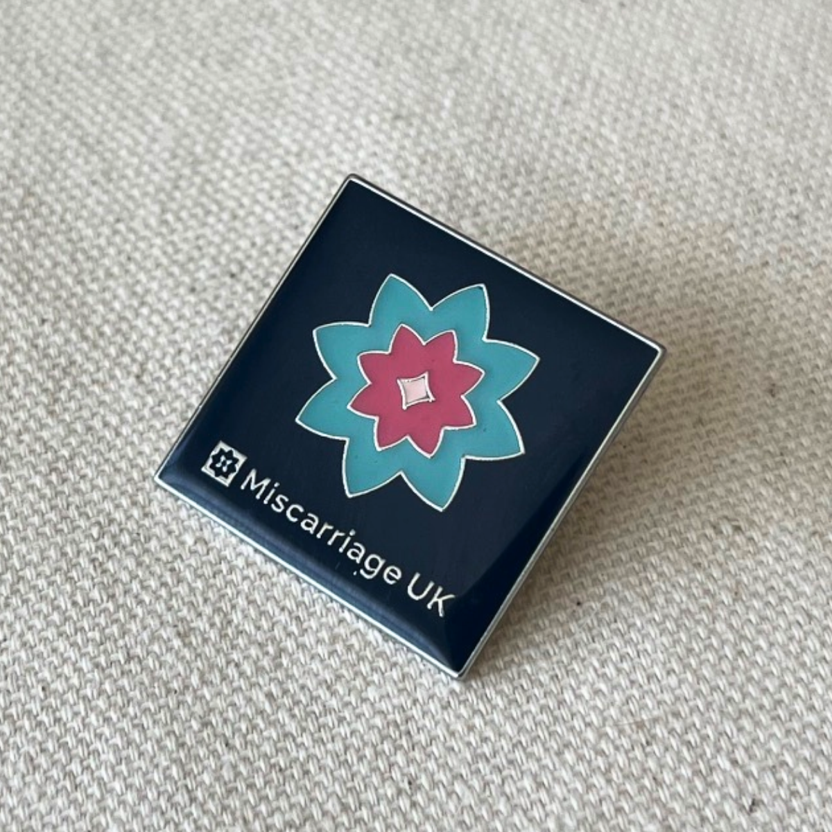 Miscarriage UK flower pin badge on cream background